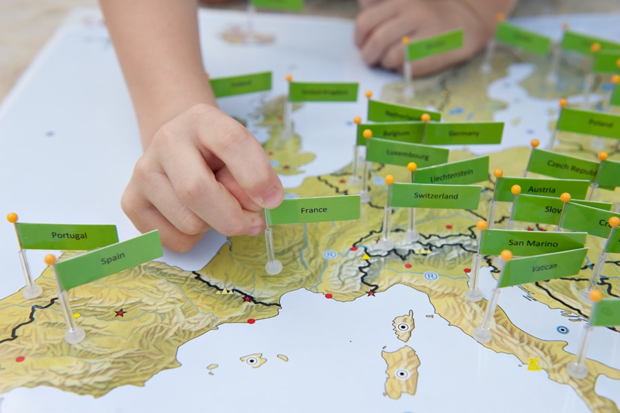 Children placing pin flags on a detailed Europe map — the original Pin It Maps product